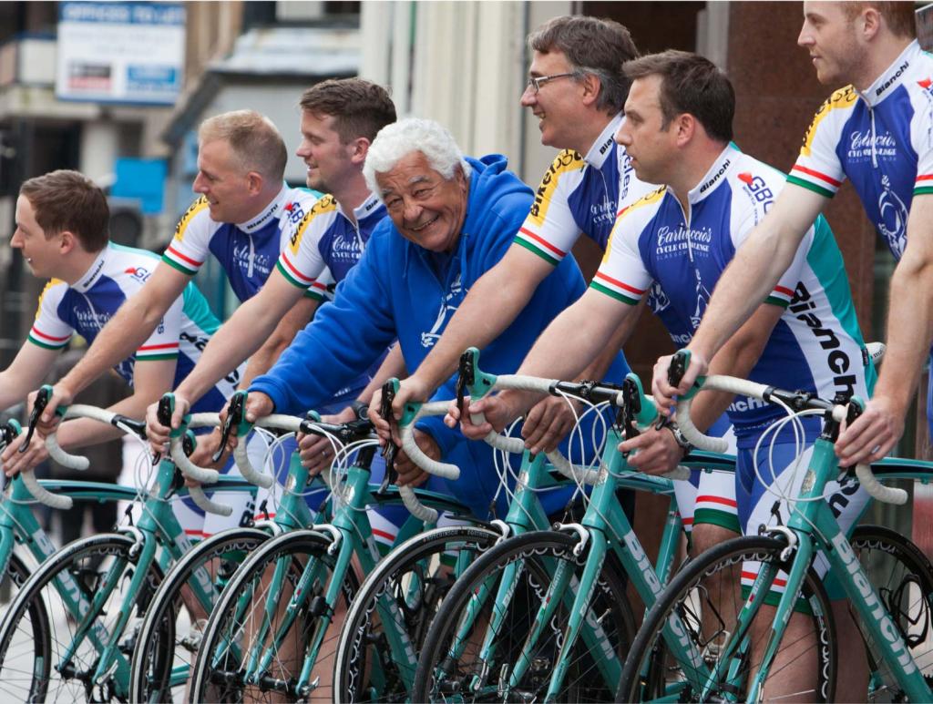 Antonio Carluccio looking at the camera with a happy smile in the middle of 6 other men looking in the other direction, all standing with their racing bicycles